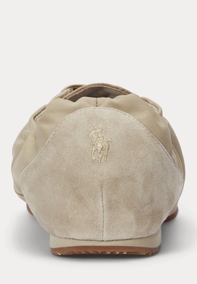 Bailarinas em camurça bege, com bico arredondado, com acabamento elástico e sola em borracha. Apresentam um logotipo em relevo no calcanhar.