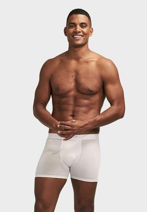 Vita boxerkalsonger i ett mjukt, stretchigt tyg. Har en bekväm midja och en figursydd design. Modellen står med händerna hopknutna.