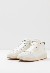 Hvide højhælede sneakers lavet af struktureret læder, med perforeret tå, guldøjer og en beige gummisål. Accentueret med logo detaljer.