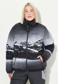Chaqueta acolchada con un patrón de montaña en blanco y negro, diseñada con un cuello alto, cremallera frontal y bolsillos laterales.