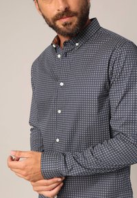Diepblauw overhemd met knopen, voorzien van een klein wit geometrisch patroon, met een kraag en lange mouwen, gemaakt van een lichte stof.