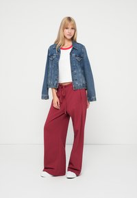 Denim jacket with a light wash, white crop top with a red neckline, and loose burgundy pants with a drawstring. White sneakers complete the look.