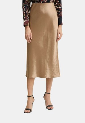 Gonna beige di media lunghezza in tessuto morbido e arricciato. Presenta una silhouette dritta e una texture liscia, abbinata a sandali neri con tacco.