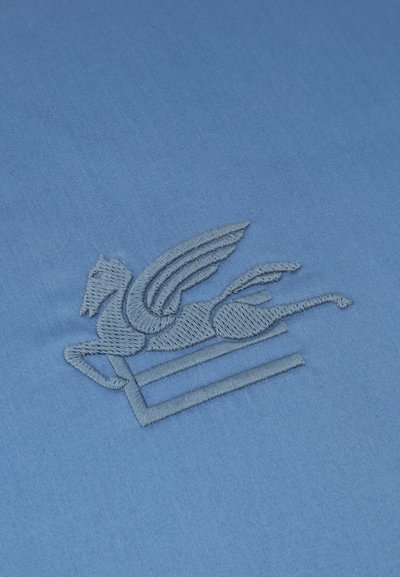 Broderie d'un cheval ailé en plein vol sur un tissu bleu lisse, montrant des coutures détaillées et la texture.