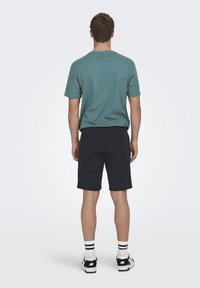 T-shirt vert pour homme à coupe décontractée, associé à un short bleu marine foncé. Il possède des manches courtes, une couleur unie et un design minimal.