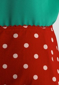 Sukienka z zieloną górną częścią i czerwoną dolną częścią. Dolna część ma duże białe kropki i falbaniasty detal na końcu.