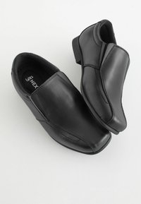 Chaussures noires en cuir à enfiler avec une texture lisse, bout pointu, couture minimale et un design à talon bas. La semelle présente un léger motif de crampons.