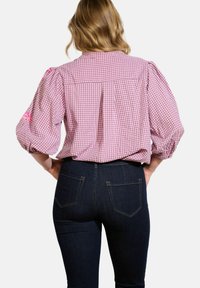 Camicia a quadretti rosa con maniche a sbuffo, con dettagli floreali. Abbinata a jeans slim blu scuro con tasche frontali.