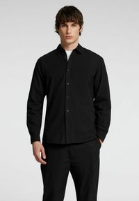 Maglietta nera a maniche lunghe con chiusura a bottoni, vestibilità su misura e una texture liscia. Abbinata a pantaloni neri per un look coordinato.