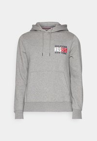 Felpa grigia con cappuccio, dotata di tasca a marsupio frontale, cappuccio con cordino, e una grafica in rosso, bianco e blu con "HILFIGER 1985 NEW YORK."