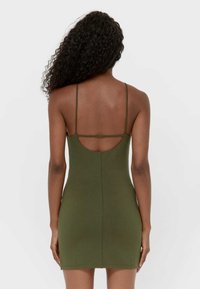 Vihreä istuva minimekko ohuilla olkaimilla, syvä takaleikkaus ja sileä, joustava kangas. Ei näkyviä kuvioita tai koristeita.