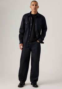 Camisa de mezclilla oscura y pantalones de pierna ancha en color navy, con una camiseta negra debajo. Presenta un frente abotonado y dos bolsillos en el pecho. Textura suave.