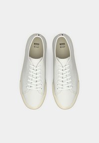 Sneakers albe din piele, cu vârf rotund, șireturi plate, talpă din cauciuc și branding subtil. Caracteristici: textură moale și design minimalist.