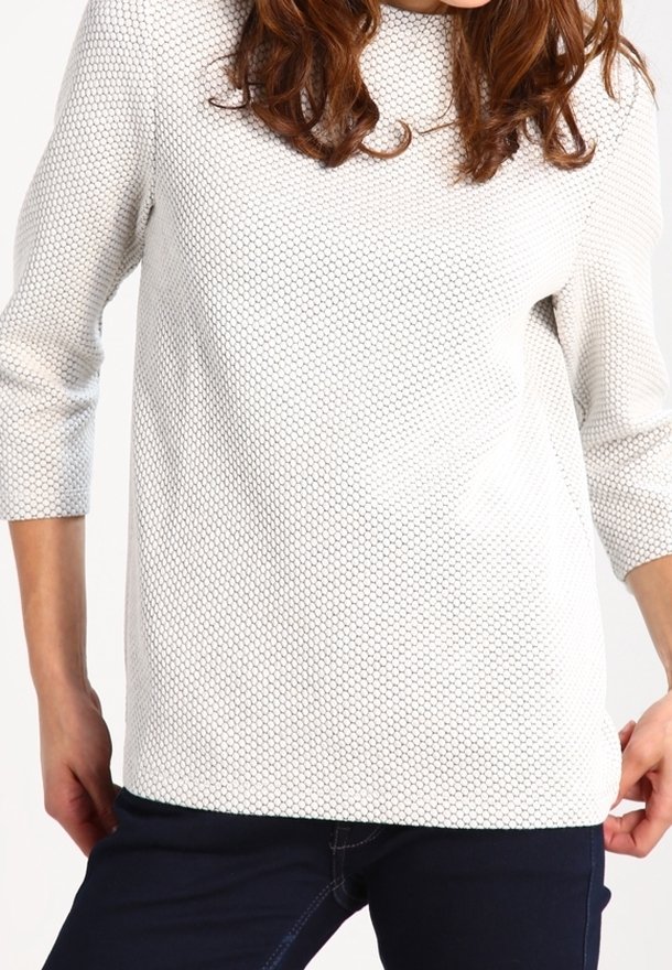 Suéter de punto texturizado en gris claro con un corte holgado, cuello redondo y mangas de tres cuartos, combinado con jeans oscuros.