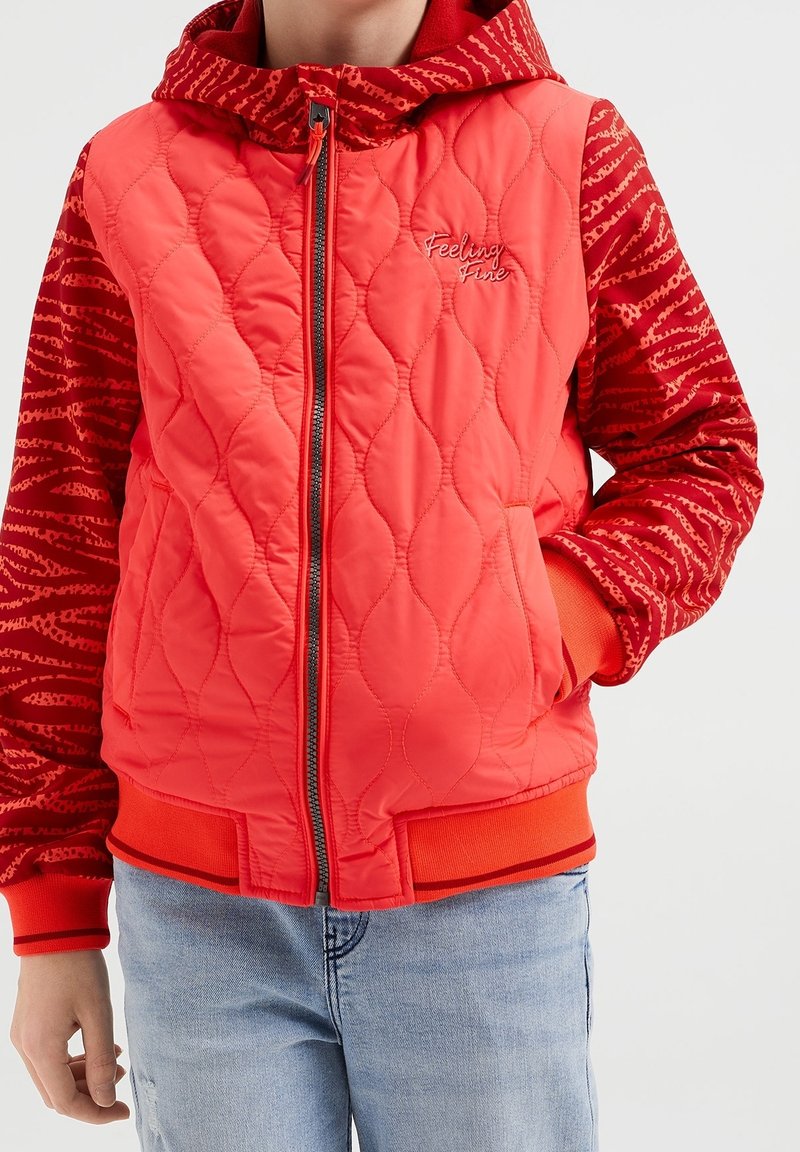 Czerwony puchowy płaszcz z pikowanym przodem, wzorzystymi czerwonymi rękawami i kapturem. Posiada zamek błyskawiczny z przodu oraz elastyczne mankiety i dół.