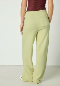 Svetlo zelene široke hlače iz mehkega materiala, z elastičnim pasom in eno zadnjo žepom. Gladka struktura in sproščen kroj.