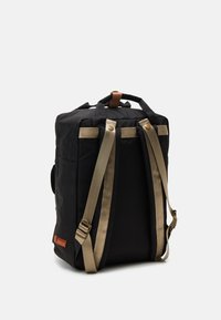 Black backpack with gold straps, fabric texture, two top handles, and a brown leather accent. Features a side pocket and adjustable straps.