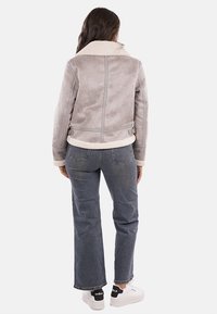 Giacca grigia in shearling sintetico con colletto morbido, tasche laterali e orlo regolabile, abbinata a jeans denim scuri e sneakers bianche.