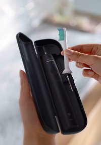 Spazzolino elettrico Philips Sonicare in una custodia nera, con una testina bianca per spazzolino caratterizzata da setole blu che viene sollevata.