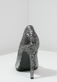 Černý třpytivý vyšší podpatek se špičatou špičkou, lesklým povrchem a štíhlým stiletto podpatkem, se solidní černou vnitřní stranou.