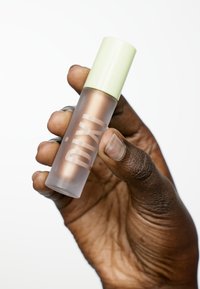 Bouteille en verre clair avec finition givr&eacute;e, remplie de bronzant. Capuchon vert, logo "pixi" en blanc bien visible. Tenue dans une main avec une texture visible.