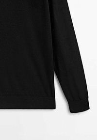 Vêtement noir à manches longues avec des poignets et un ourlet côtelés. Texture lisse, design minimaliste sans ornements ni motifs.