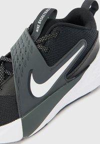 Čierna športová obuv s plastovou vrchnou časťou, šedými detailmi, textúrovaným remienkom a výrazným bielym logom Nike na boku.