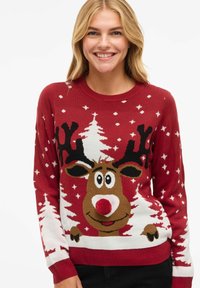 Punane kootud sviiter, millel on põhjapõdra disain pom-pomi ninaga, ümbritsetud valgetest puudest ja lumehelbedest. Pika varrukaga ja soonikuga mansetid.