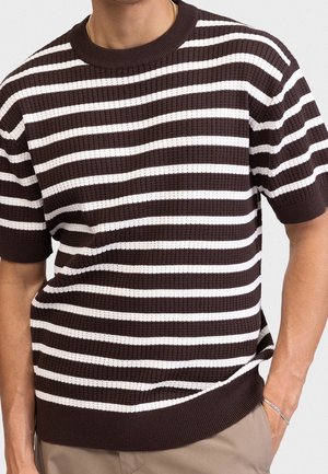 Mann trägt braun-weiß horizontal gestreiftes Kurzarm-Strickshirt mit beiger Hose, goldener Halskette und silbernem Armband.