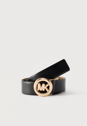 Črni usnjeni pas, zvit z okroglo zlato sponko z logotipom "MK" na sredini na enostavni svetli podlagi.