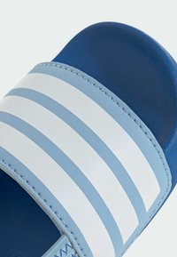 Blue slide sandal featuring a textured upper strap with three white horizontal stripes, and a smooth blue footbed. Stitched accents detail.