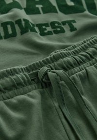 Grüne Baumwoll-Sweatpants mit einem gerafften, elastischen Bund und Kordelzug, weichem Stoff und boldem, in dunklerem Grün aufgedrucktem "MIDWEST".