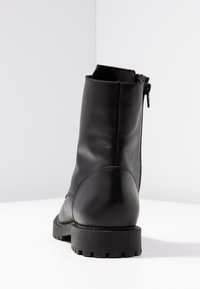 Botte de cheville en cuir noir, avec une finition lisse, un embout arrondi et une fermeture éclair à l'arrière. Équipée d'une semelle robuste avec un motif de crampons prononcé.