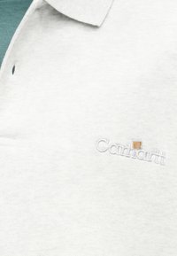 Λευκό πόλο πουκάμισο Carhartt WIP με γιακά, μερικώς εμφανιζόμενο από το πάνω μέρος και κεντημένο λογότυπο στην αριστερή πλευρά του στήθους.