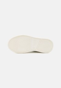 Suola di una sneaker, caratterizzata da una superficie in gomma bianca testurizzata con linee curve e un dettaglio rettangolare incorporato vicino al tallone.