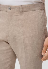 Tan geruite broek van lichtgewicht stof, met een gladde voorkant, standaard tailleband en zijzakken. Knopen sluiting zichtbaar.