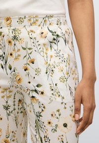 Παντελόνια από ύφασμα με λουλουδένιο σχέδιο σε εκρού χρώμα, με κίτρινες και πράσινες βοτανικές διακοσμήσεις, ελαστική μέση και πλαϊνές τσέπες. Απαλή υφή.