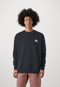 Marinblå sweatshirt med långa ärmar, ribbade muddar och rund halsringning. Har en liten vit grafik på bröstet. Mjuk textur.