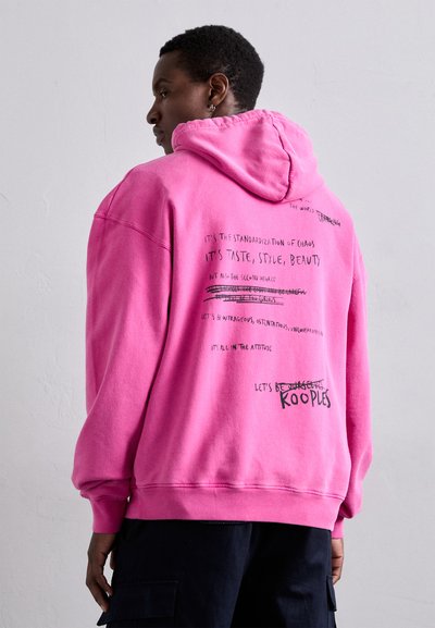 Pink hoodie with a relaxed fit, featuring printed text on the back, including bold phrases and crossed-out words. Ribbed cuffs and hem.