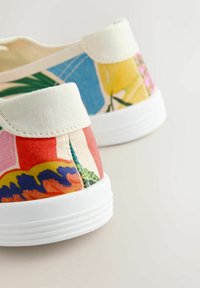 Zbliżenie na dwie kolorowe, wsuwane buty z płótna z białymi podeszwami i wielokolorowymi wzorami kwiatowymi oraz abstrakcyjnymi.