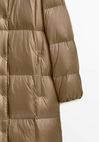 Giacca imbottita di colore marrone chiaro, con un design trapuntato, tasca con zip, texture liscia e bottoni a pressione circolari.