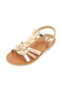 Sanda con una plantilla de cuero marrón, correas trenzadas doradas y acentos metálicos. Cuenta con una correa ajustable en el tobillo con hebilla.