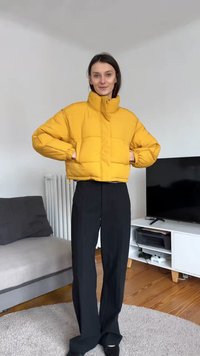 Chaqueta acolchada amarilla con cuello alto, textura acolchada y puños elásticos; combinada con pantalones negros de pierna ancha. Mobiliario suave en el fondo.