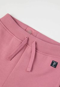 Lyserøde sweatpants har en ribbet talje med en knap, snoretræk og et lille logo mærke. Teksturen er blød og glat.