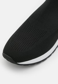 Svart sportskor med andningsbar stickad ovandel, med texturerad yta och vit mellansula. Rundad tå och flexibel gummisula.