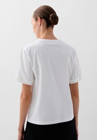 Hvid bomulds T-shirt med korte ærmer og rund halsudskæring, der har en afslappet pasform og en glat tekstur, vist fra ryggen.