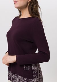 Langarmtop in diepe paarse katoenmix, met een ronde halslijn en een geborduurde zoom met cirkelvormige ontwerpen en zilveren accenten.