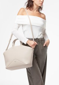 Borsa a mano in pelle beige con un design geometrico, finitura testurizzata, due manici e una tracolla regolabile, tenuta da una persona.