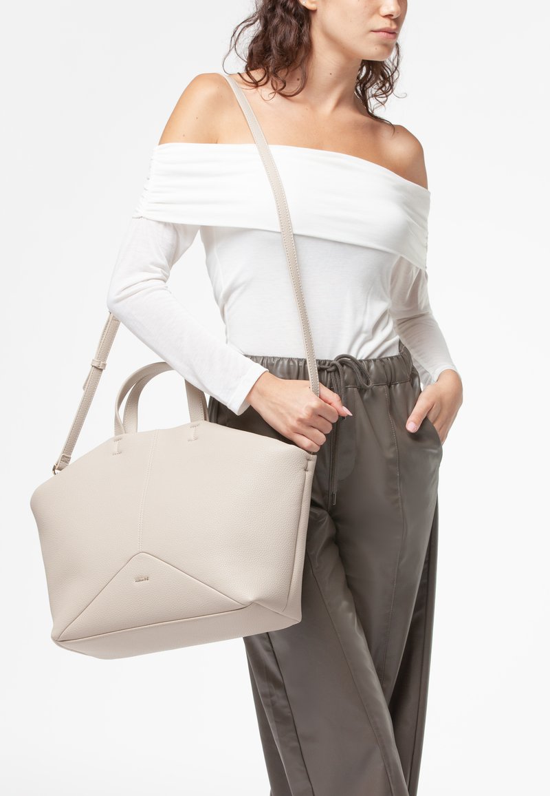Borsa a mano in pelle beige con un design geometrico, finitura testurizzata, due manici e una tracolla regolabile, tenuta da una persona.