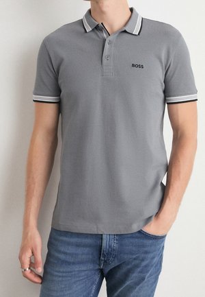 Camisa polo gris con cuello y puños a rayas blancas y negras; presenta un pequeño logo negro en el pecho; hecha de tela texturizada.